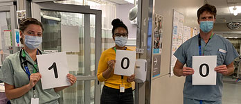 Three hospital staff holding up signs spelling out the number 100