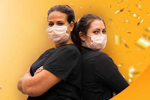 Two women standing back to back wearing masks
